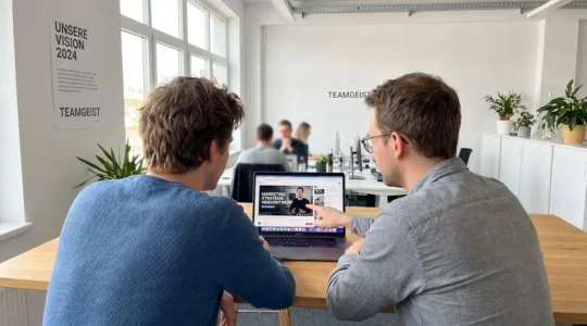 Zwei Marketing-Profis arbeiten zusammen an einem Laptop in einem hellen modernen Büro und überprüfen Videoinhalte