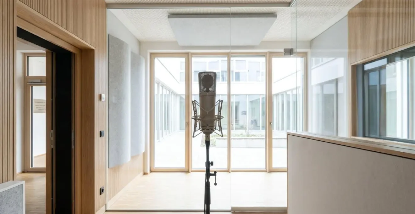 Weitwinkelaufnahme eines leeren modernen Aufnahmestudios mit professionellem Mikrofon, klarem zeitgenössischem Design und natürlichem Licht
